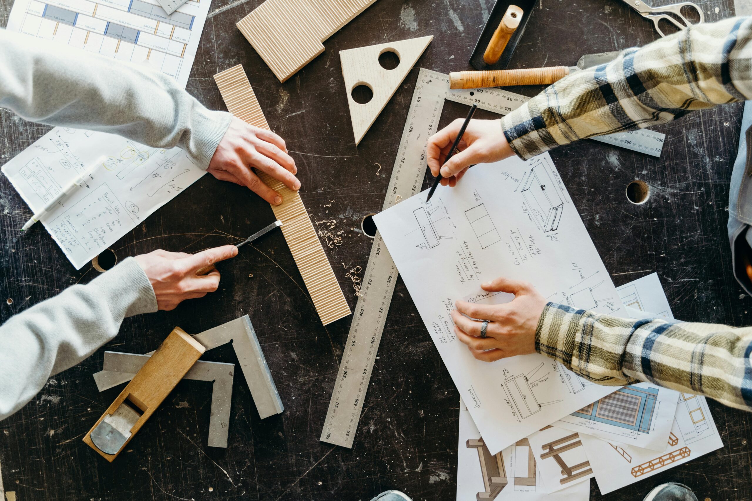 Top view of two people designing and crafting woodworking projects with blueprints and tools.